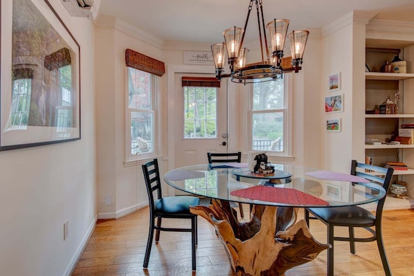 A dining area with a glass table, black chairs, a wooden tree stump centerpiece, and a chandelier. - The Wander Inn (Blowing Rock)