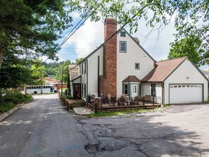 A two-story building with a brick chimney, a garage, and a porch with chairs.
