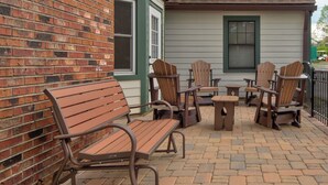 An outdoor patio with wooden Adirondack chairs and tables, a brick wall, and a building with a green door and window. - The Wander Inn (Blowing Rock)