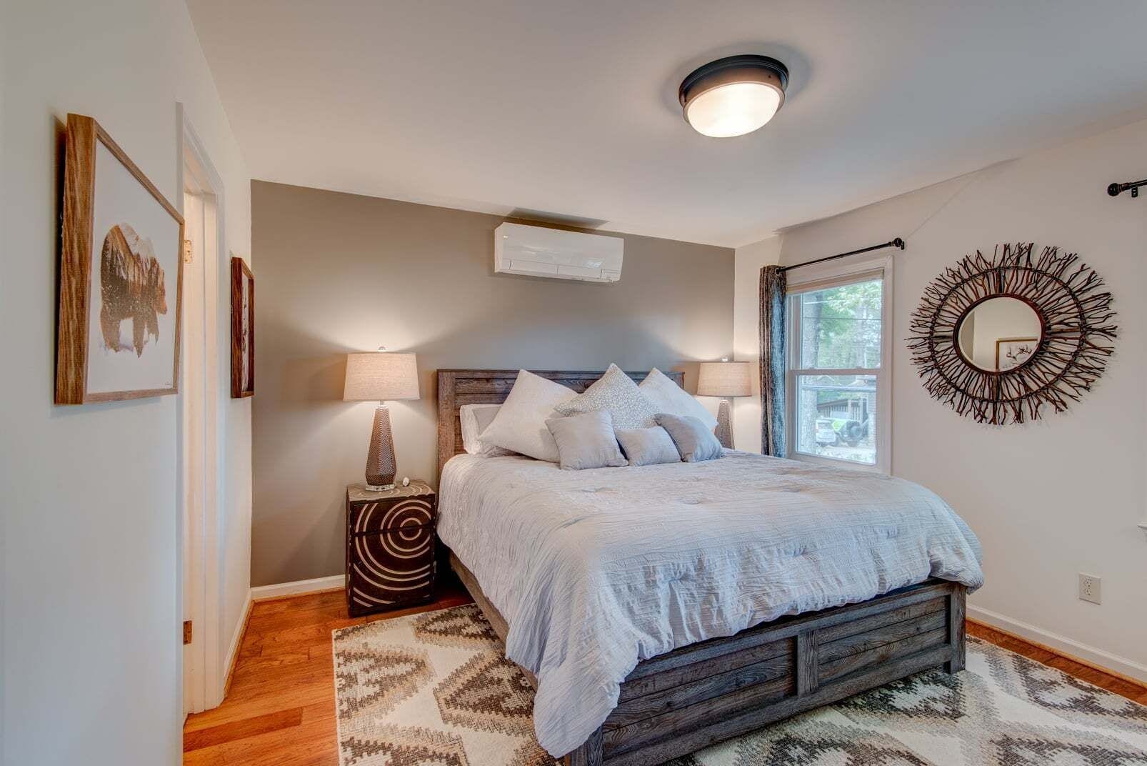 A bedroom with a bed, bedside lamps, a window, a wall-mounted mirror, and a ceiling light fixture.