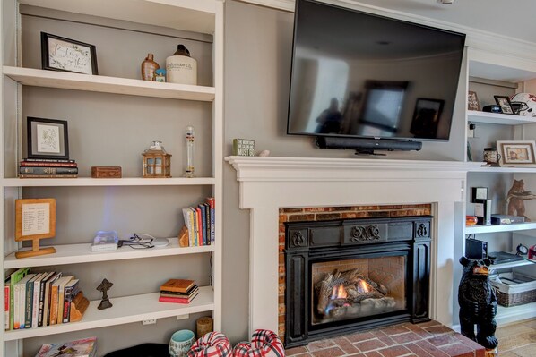 A living room with a fireplace, bookshelves, and a flat-screen TV mounted above the fireplace.