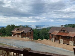 Two rustic cabins with stone foundations and metal roofs, surrounded by a gravel driveway and a forested landscape. - The Roper Retreat at Eagles Nest (Banner Elk)