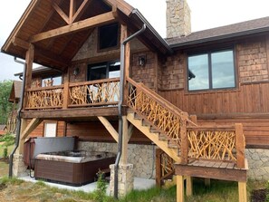 A wooden cabin with a stone chimney, a hot tub, and a wooden staircase. - The Roper Retreat at Eagles Nest (Banner Elk)