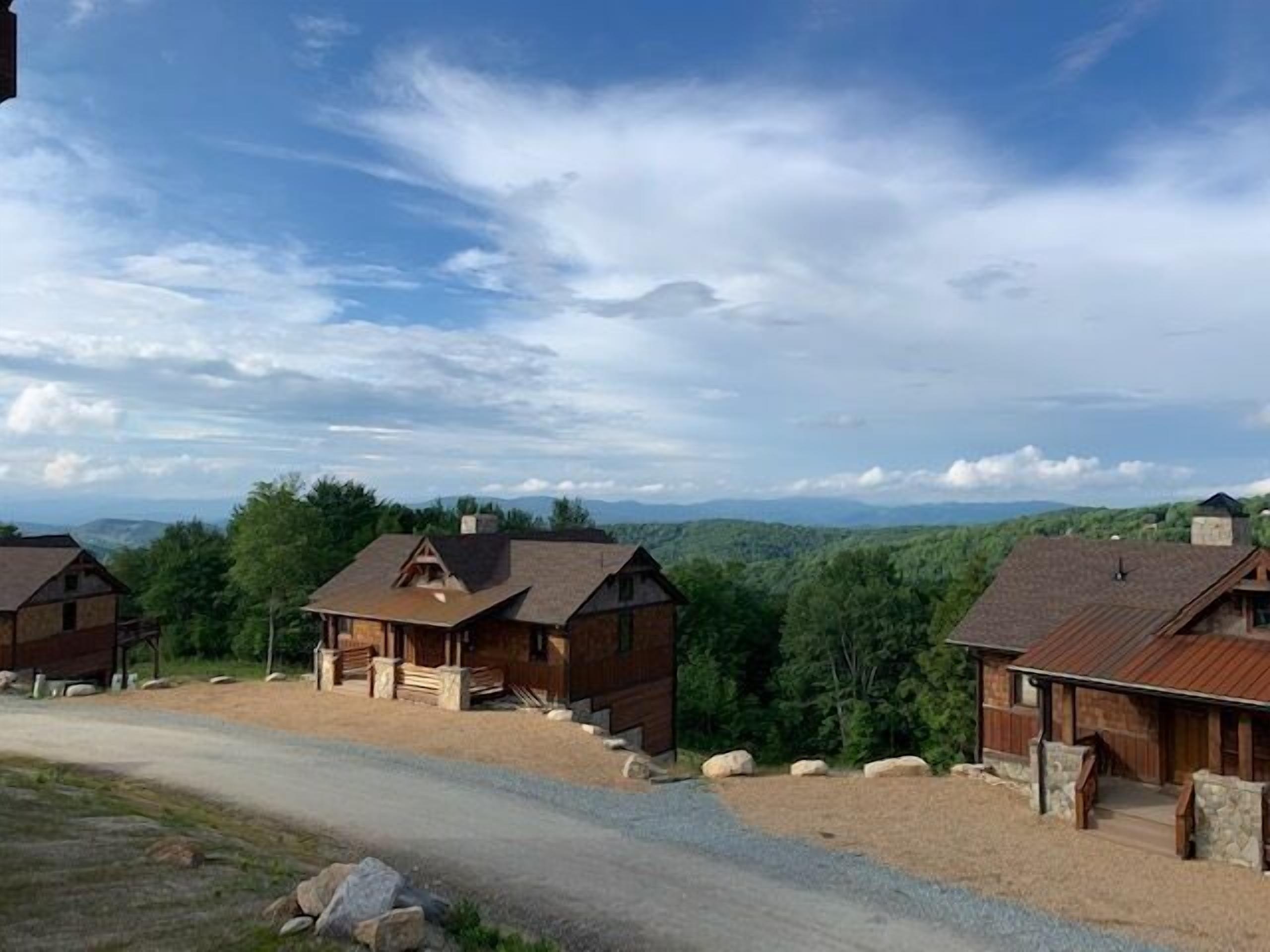 A row of log cabins with a gravel driveway and a view of the mountains in the background.
