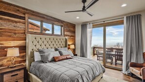 A bedroom with a large bed, a ceiling fan, a nightstand, a lamp, and a view of an outdoor deck. - Eagle Rare Retreat at Eagles Nest (Banner Elk)
