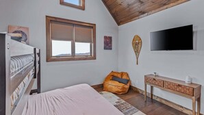 A bedroom with a bed, a window, a television, a wooden ceiling, and a small seating area. - Eagle Rare Retreat at Eagles Nest (Banner Elk)