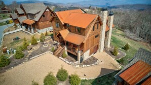 A large wooden cabin with a stone chimney, surrounded by a well-maintained lawn and a view of distant mountains. - Eagle Rare Retreat at Eagles Nest (Banner Elk)