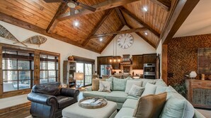 Un salon spacieux avec un grand canapé d’angle, un fauteuil en cuir et un plafond en bois avec des poutres apparentes.