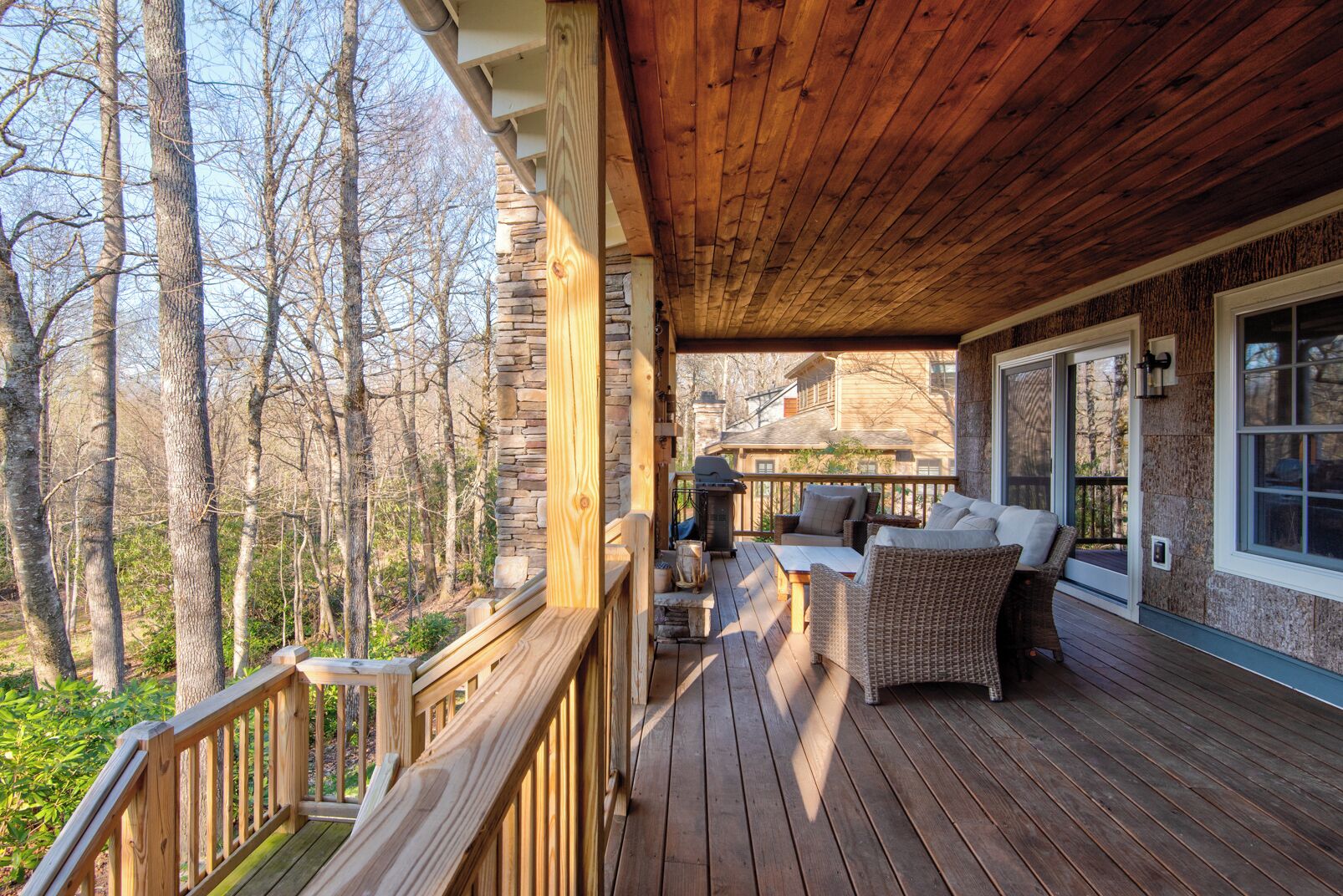 Eine Holzterrasse mit einer Steinmauer, Gartenmöbeln und Blick auf den umliegenden Wald.