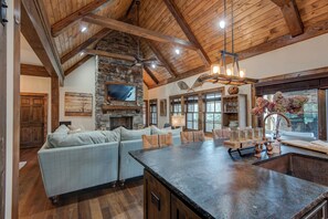 A spacious living area with a stone fireplace, a large sofa, and a dining table. - Bluebird Cottage at Sweetgrass (Blowing Rock)