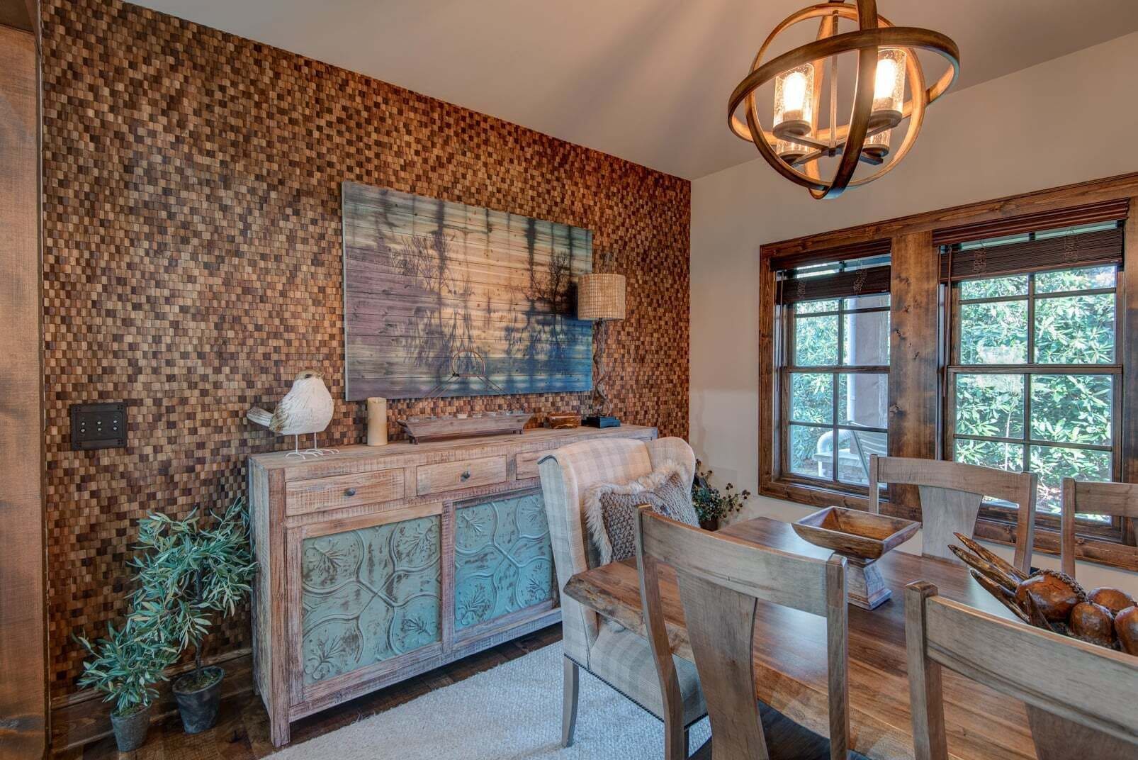 A rustic dining area with wooden furniture, a large painting on the wall, and a window with a view of greenery.