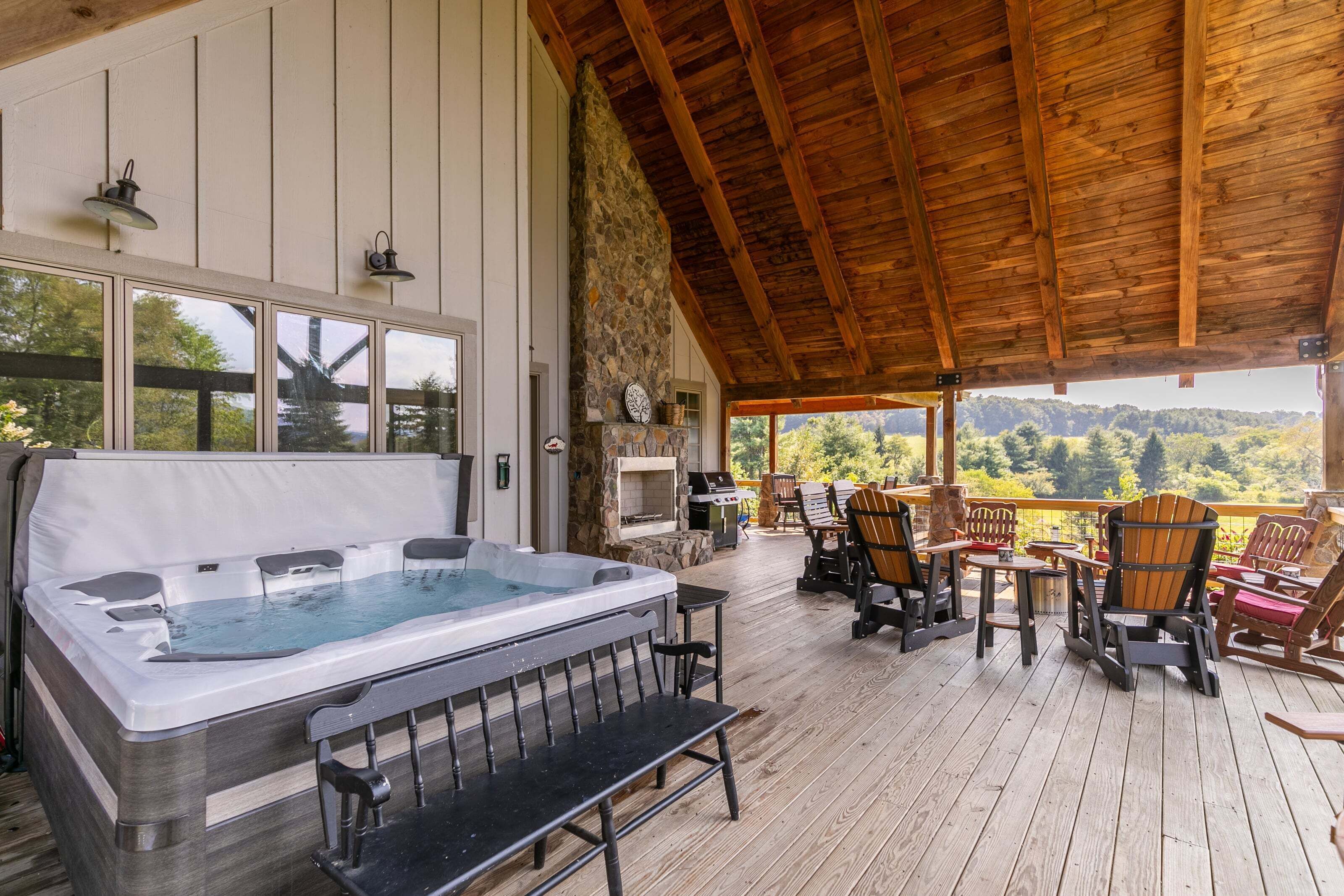 A hot tub on a wooden deck with outdoor seating and a stone wall.