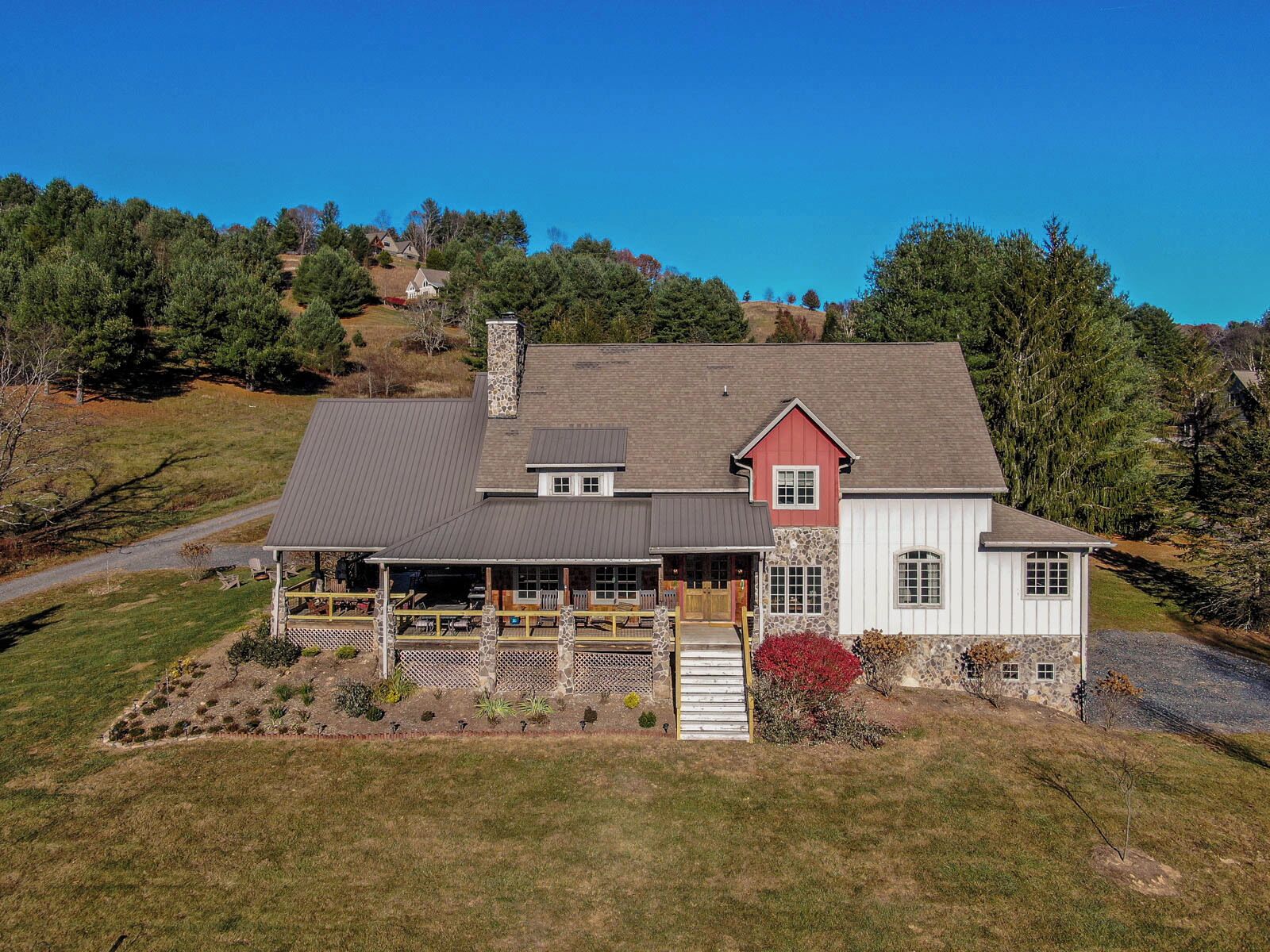A two-story house with a large porch, stone chimney, and a red and white exterior.