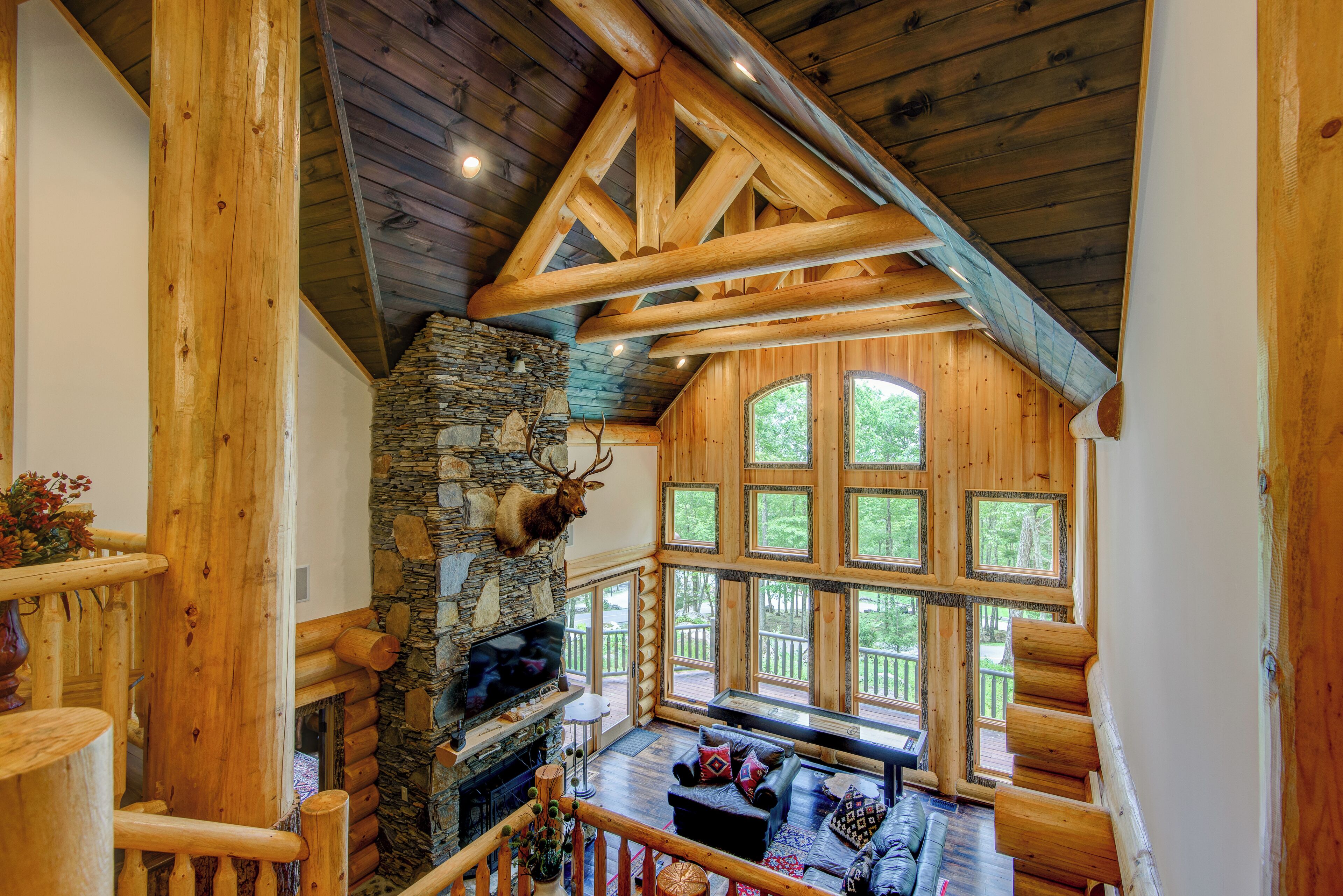 L’intérieur d’une cabane en rondins, avec une cheminée en pierre, des poutres en bois et de grandes fenêtres.