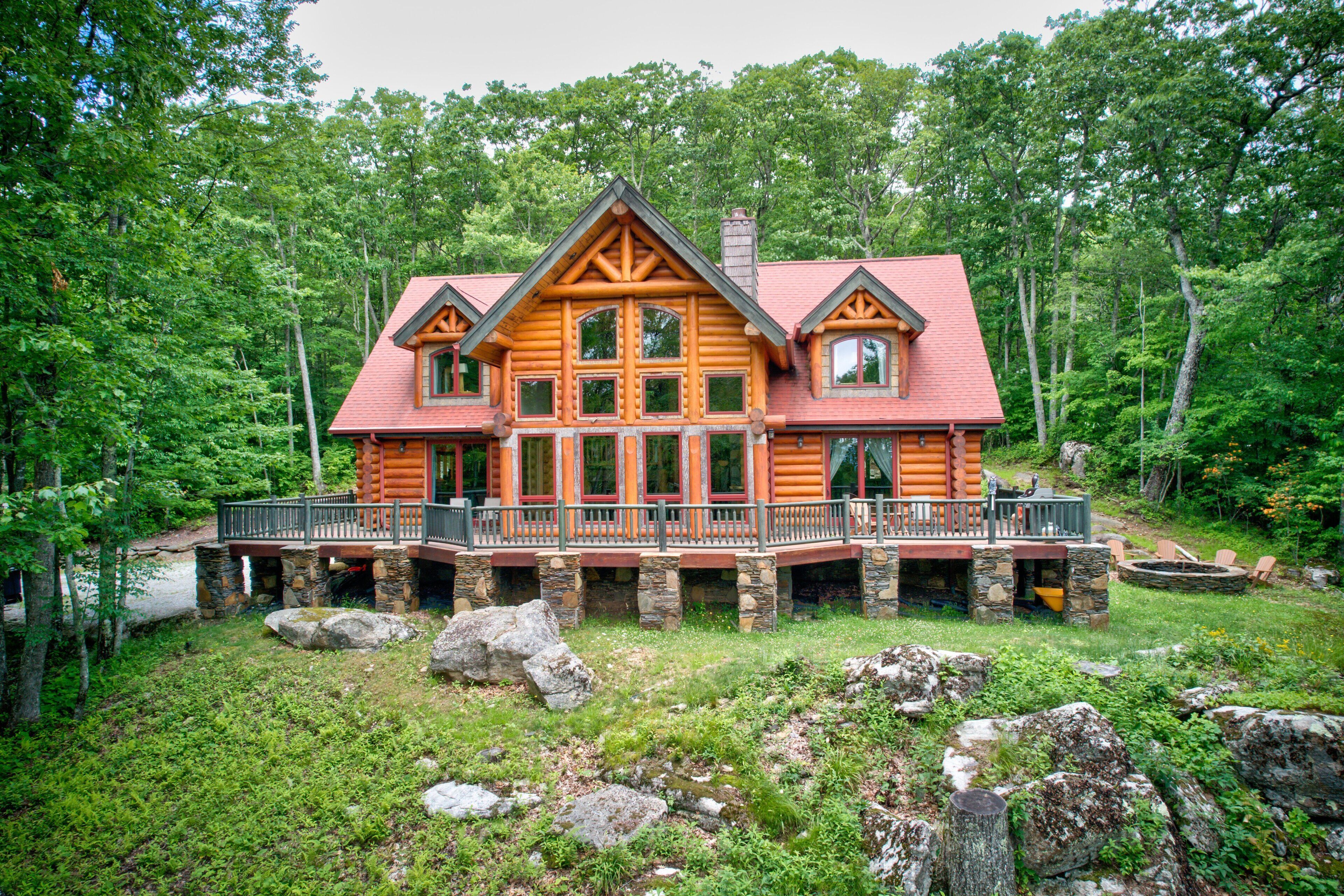 A log cabin with a balcony, surrounded by a forest.