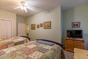 A bedroom with two beds, a ceiling fan, a television on a wooden cabinet, and several framed pictures on the wall.