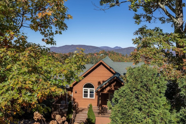 A cabin with a wooden exterior, a porch, and a mountain backdrop.