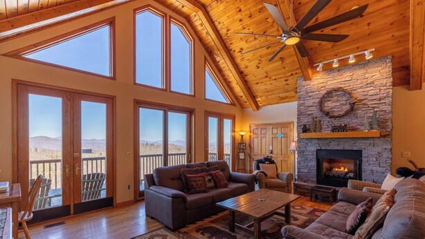 A spacious living room with a fireplace, large windows, and a high ceiling fan.