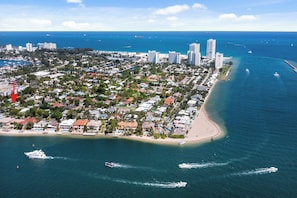 Eine Luftaufnahme einer Küstenstadt mit dicht bebauten Wohngebieten, einem Strand und einem Yachthafen mit Booten.