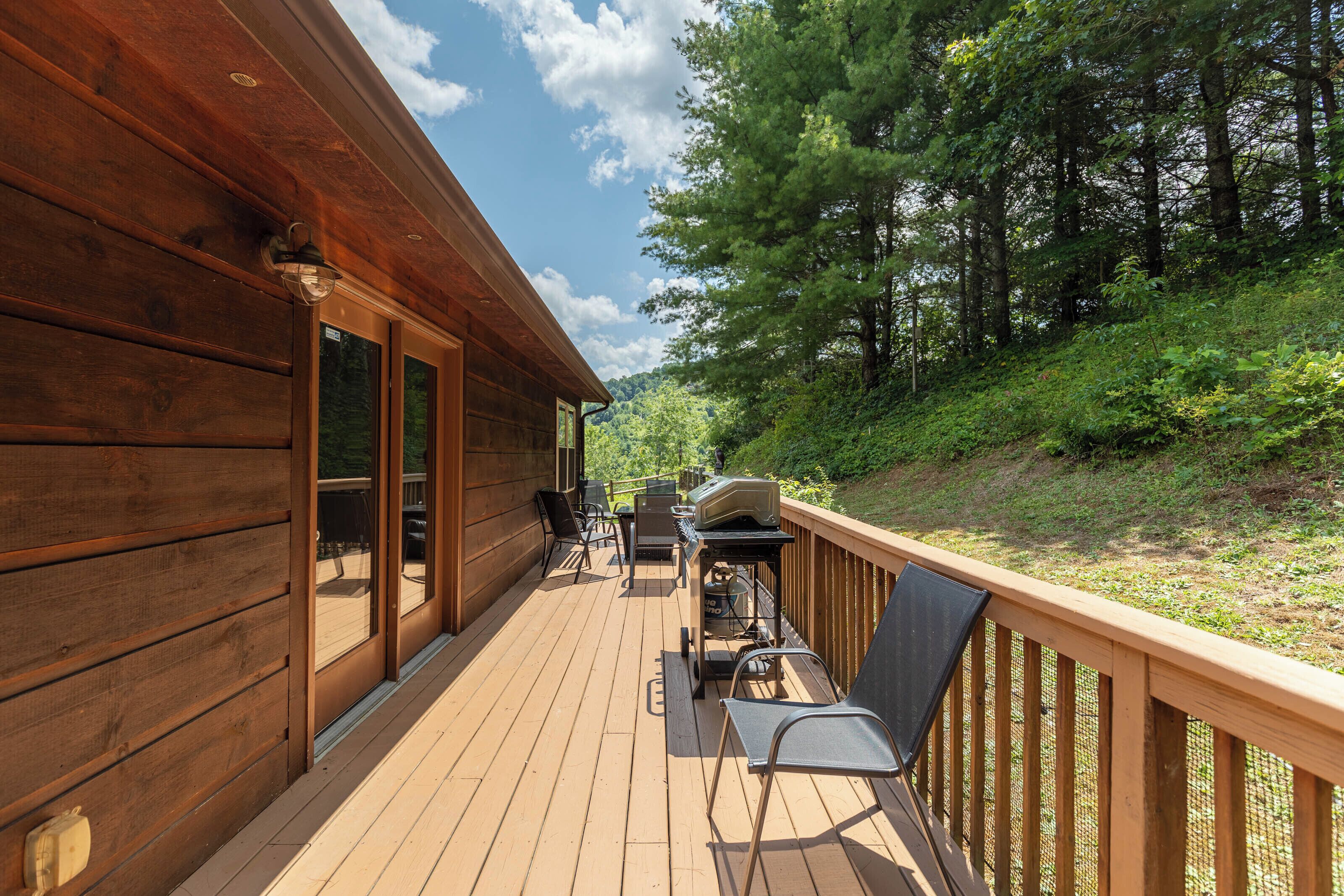A wooden deck with outdoor furniture, a grill, and a view of a forested hillside.
