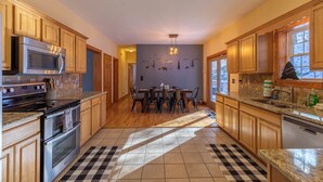 A kitchen with wooden cabinets, a granite countertop, a built-in microwave, and a dining area with a table and chairs. - Lazy Bear Inn (Sugar Grove)