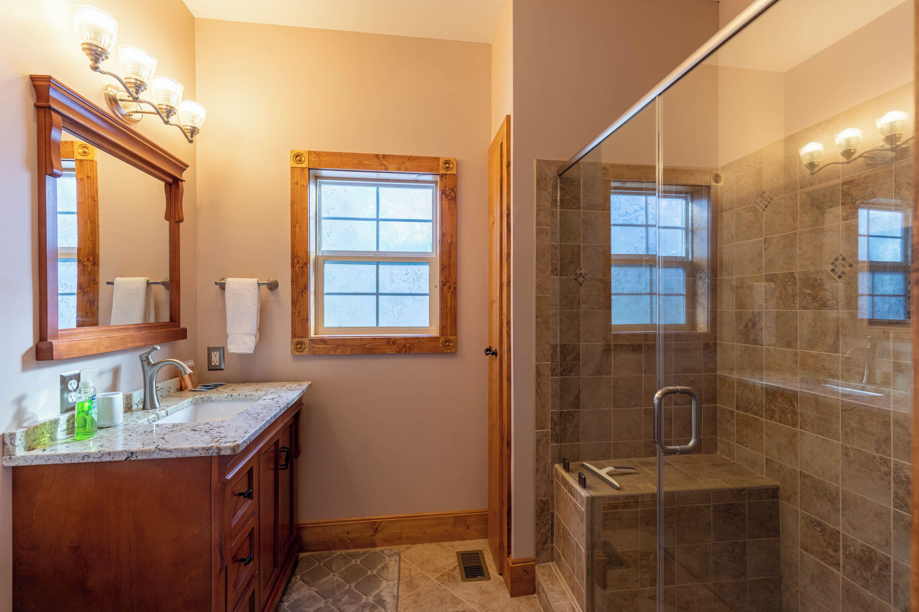 A bathroom with a wooden vanity, a glass-enclosed shower, and a window.