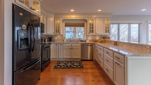 A modern kitchen with white cabinetry, stainless steel appliances, and a large window providing natural light. - Blue Ridge Vista (Banner Elk)