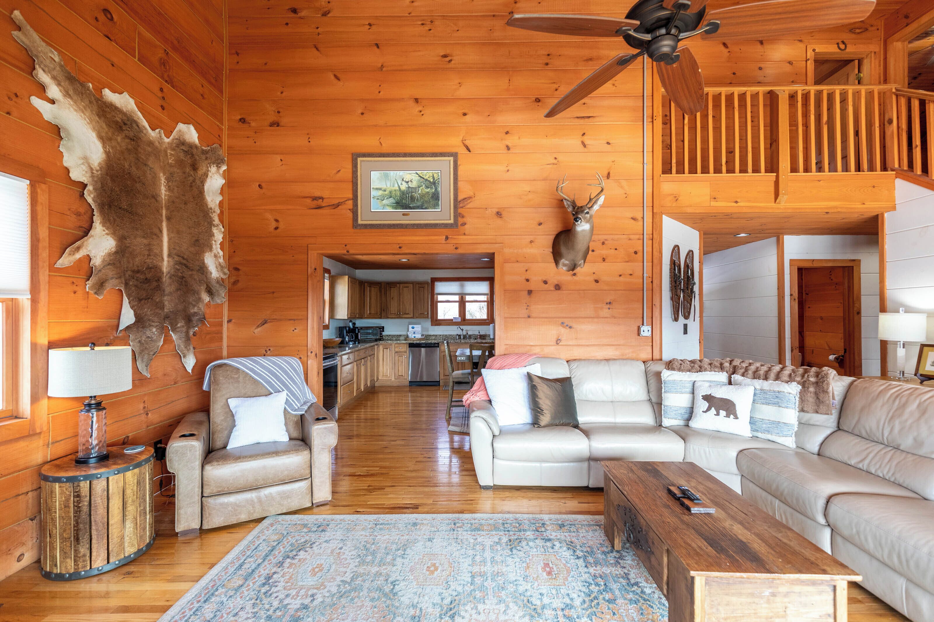 A log cabin interior with a living room, kitchen, and a ceiling fan.