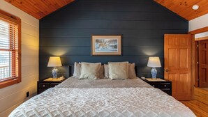 Un dormitorio con una cama grande, dos mesitas de noche con lámparas, un cuadro en la pared y una puerta de madera.