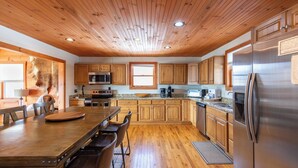 Una cocina con armarios de madera, un refrigerador de acero inoxidable y un comedor con una mesa y sillas de madera.