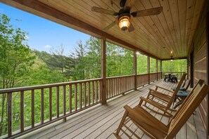 A wooden deck with a railing, wooden rocking chairs, and a table with chairs.