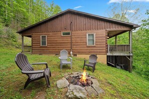 A cabin with a fire pit, two Adirondack chairs, and a deck.