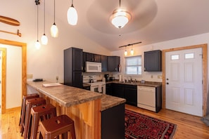A kitchen with a central island, bar stools, a microwave, stove, and a dishwasher. - Watauga River Retreat (Sugar Grove)