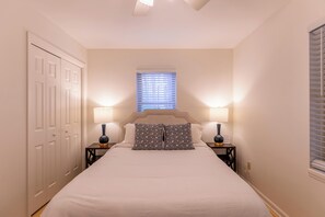 A bedroom with a bed, two bedside tables with lamps, a window with blinds, and a wardrobe.