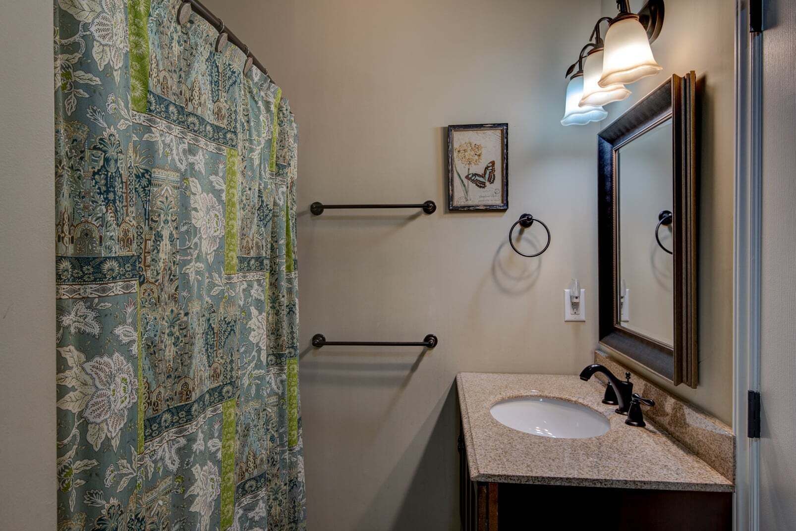 A bathroom with a patterned shower curtain, a sink with a mirror, and a wall-mounted light fixture.