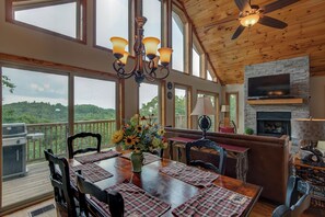 A spacious dining area with a wooden table, chairs, and a chandelier. There is a fireplace and a television mounted on the wall. - 1 Beautiful View (Blowing Rock)