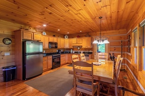 A wooden cabin interior with a kitchen, dining area, and a large window. - Amen Corner Close to Boone! Hot Tub, Pet Friendly, Ping Pong, Foosball, Mountain Views (Vilas)