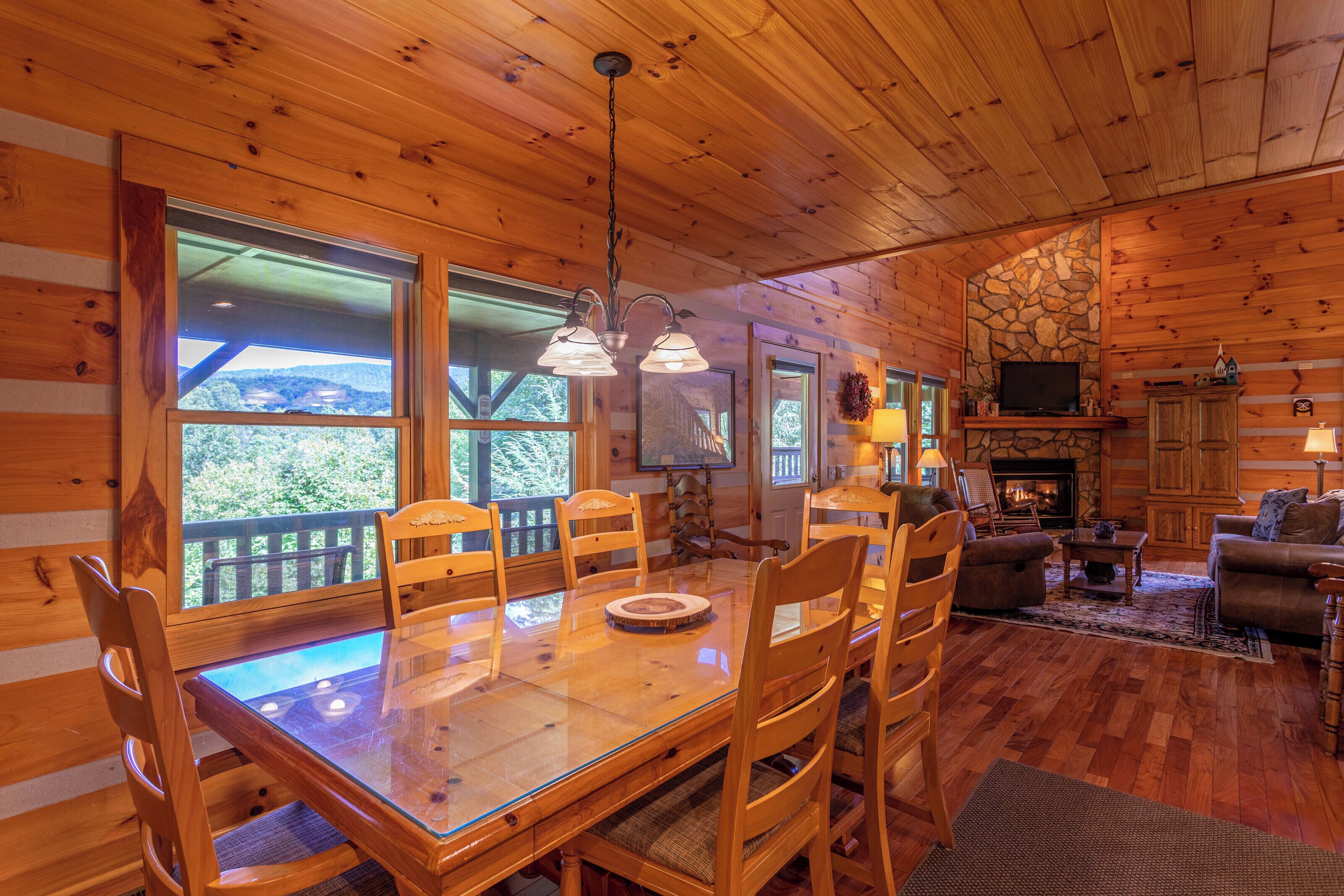 A wooden cabin interior with a dining area, living room, and stone fireplace.