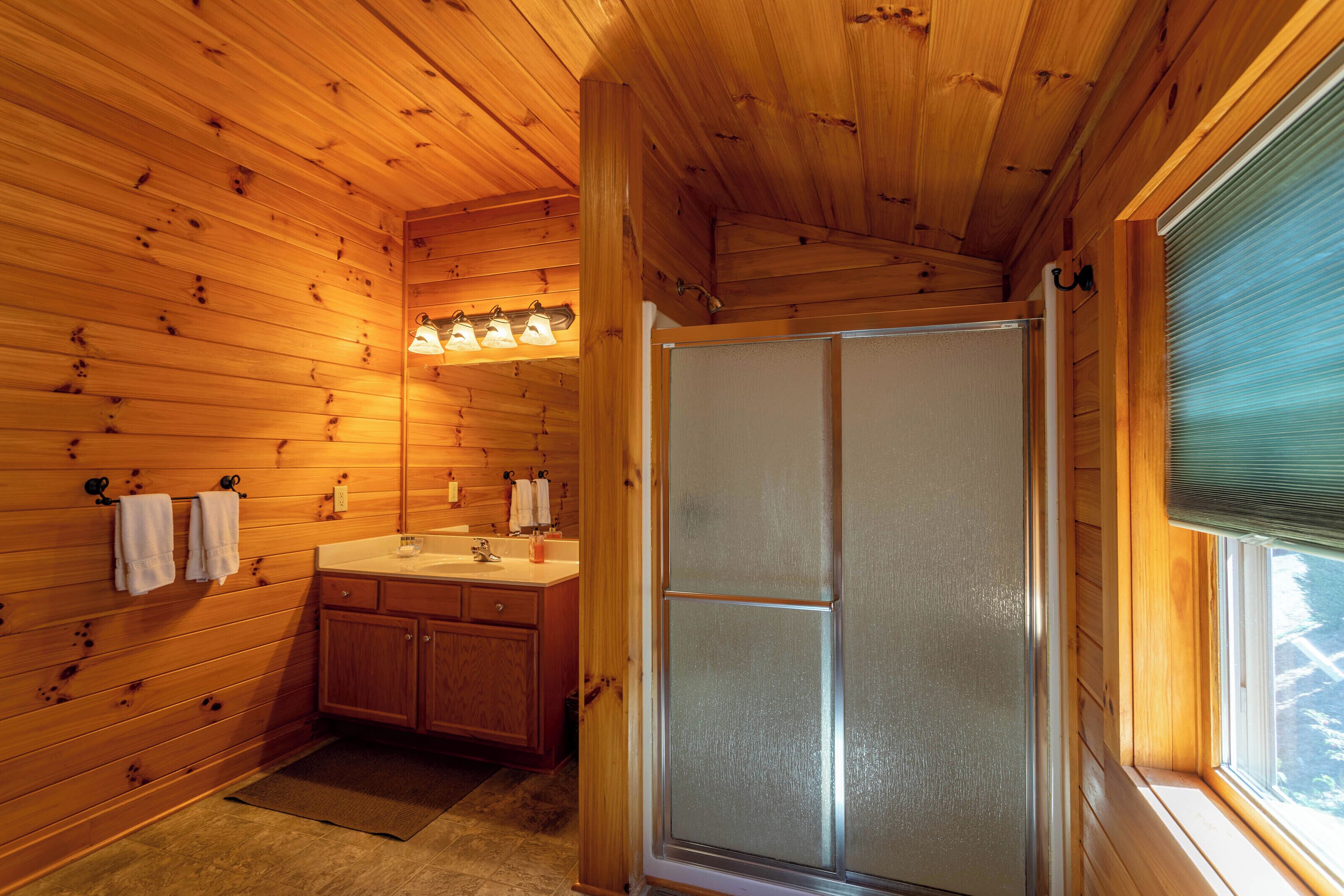 Une salle de bain rustique, aménagée dans une cabane en bois, avec une douche, un lavabo et des placards.