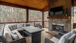 A covered outdoor area with a stone fireplace, a flat-screen TV, and comfortable seating. - Overlook Nook at Eagles Nest (Elk Park)