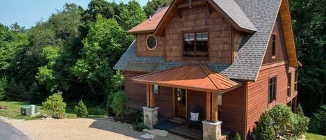 A wooden cabin with a gabled roof, a front porch, and a circular window.