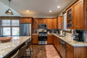 A modern kitchen with wooden cabinets, stainless steel appliances, granite countertops, and a large window.