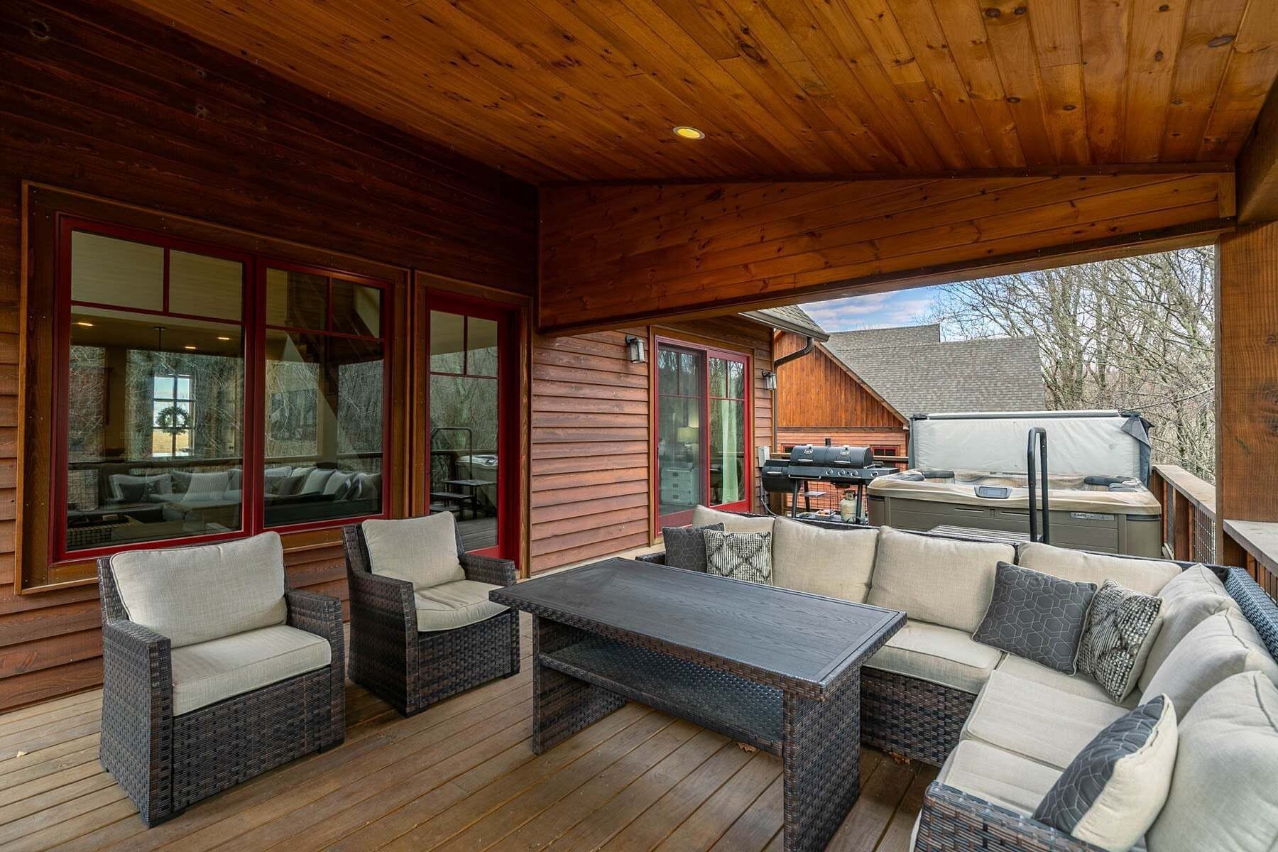 A covered outdoor seating area with wicker furniture, a grill, and a view of the surrounding landscape.