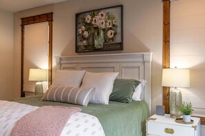 A bedroom with a bed, two bedside lamps, a nightstand with a clock, and a painting above the bed. - Overlook Nook at Eagles Nest (Elk Park)
