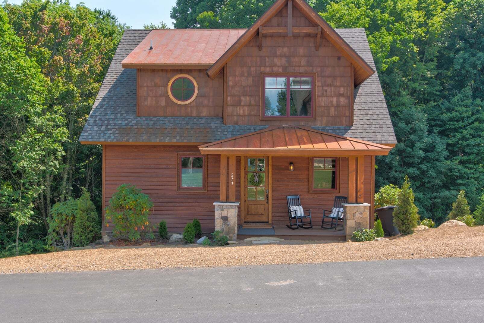 Une cabane en rondins à deux étages, dotée d’un porche à l’avant, de deux fenêtres et d’une cheminée.