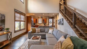 A spacious living area with a large gray sectional sofa, a wooden coffee table, and a staircase with a wooden railing. - Overlook Nook at Eagles Nest (Elk Park)