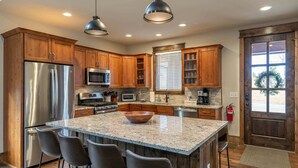A kitchen with wooden cabinets, stainless steel appliances, a granite countertop, and a large island with bar stools. - Overlook Nook at Eagles Nest (Elk Park)