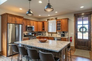 Una cocina con gabinetes de madera, electrodomésticos de acero inoxidable, encimera de granito y una isla grande con taburetes de bar.