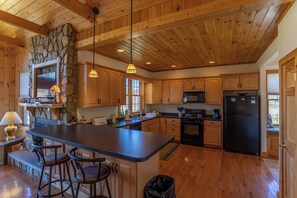 Eine geräumige Küche mit Holzschränken, einer großen Kochinsel mit Barhocker, einer Wand mit Steinakzenten und einem schwarzen Kühlschrank.