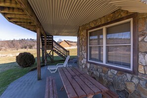 Ein überdachter Außenbereich mit einem Steinhaus, einer Holzbank und einer Treppe, die zu einer Holzkonstruktion führt.